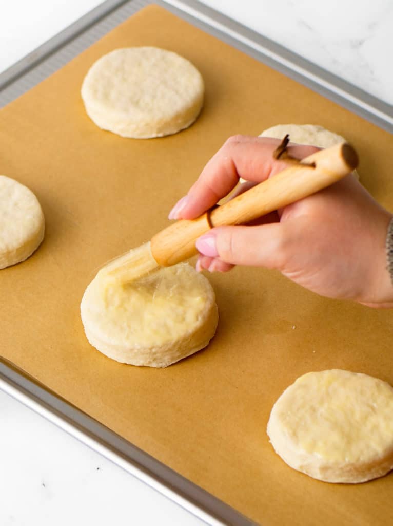 Brushing melted butter onto biscuit rounds.