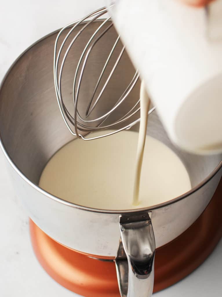 Heavy cream being poured into stand mixer bowl.