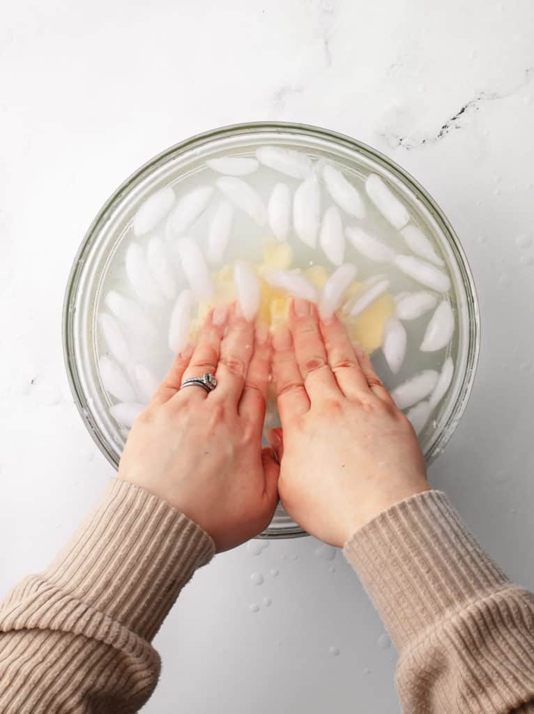 Butter transferred to a large bowl full of ice water. Using both hands to ring out excess buttermilk and clean the butter.