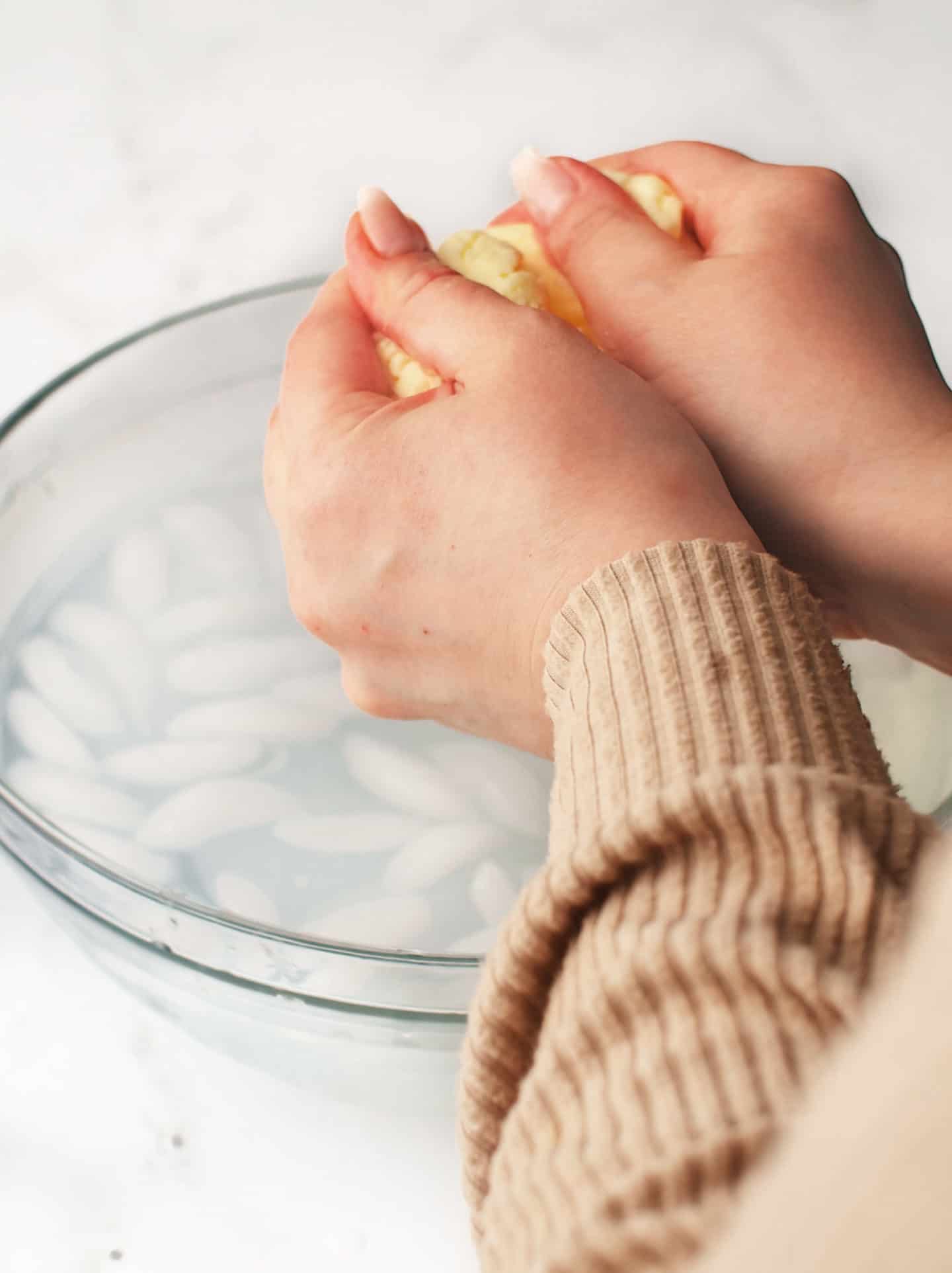 Squeezing and kneading butter in large bowl of ice water with both hands to remove excess buttermilk.