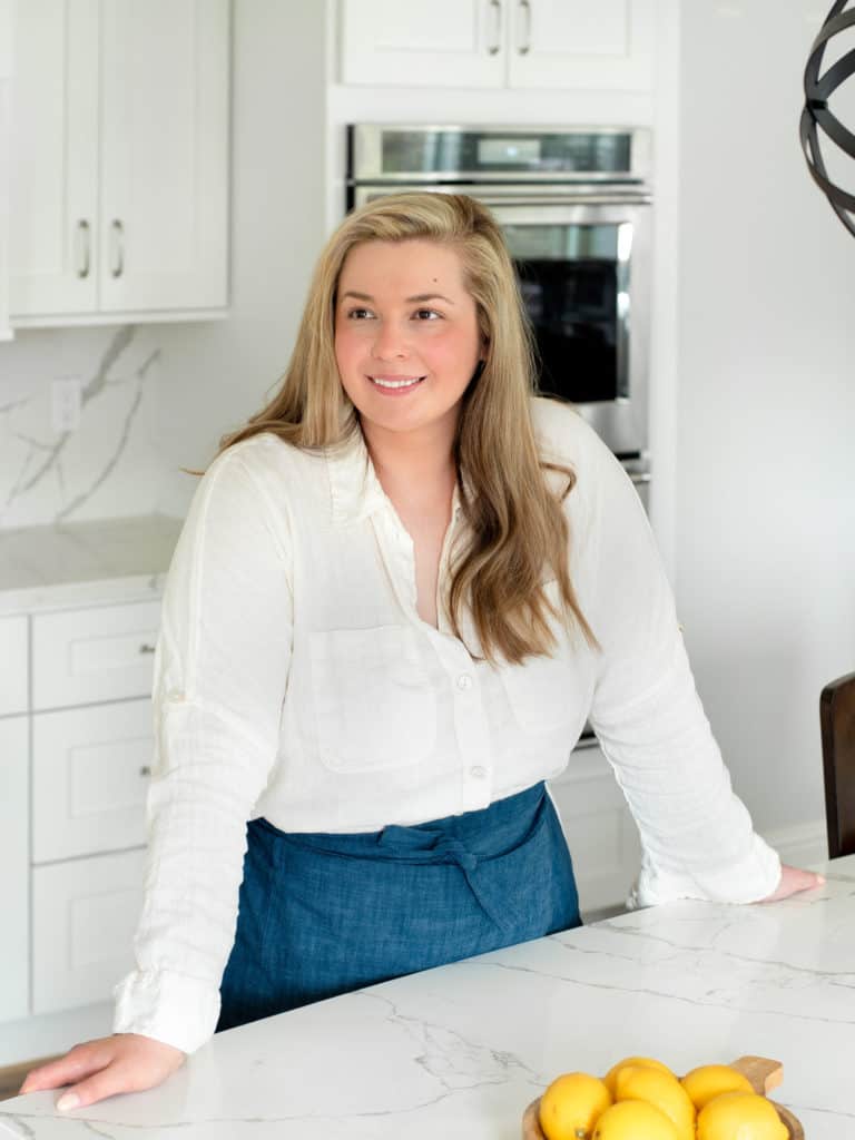 Patricia standing over the kitchen island wearing a white button up smiling.