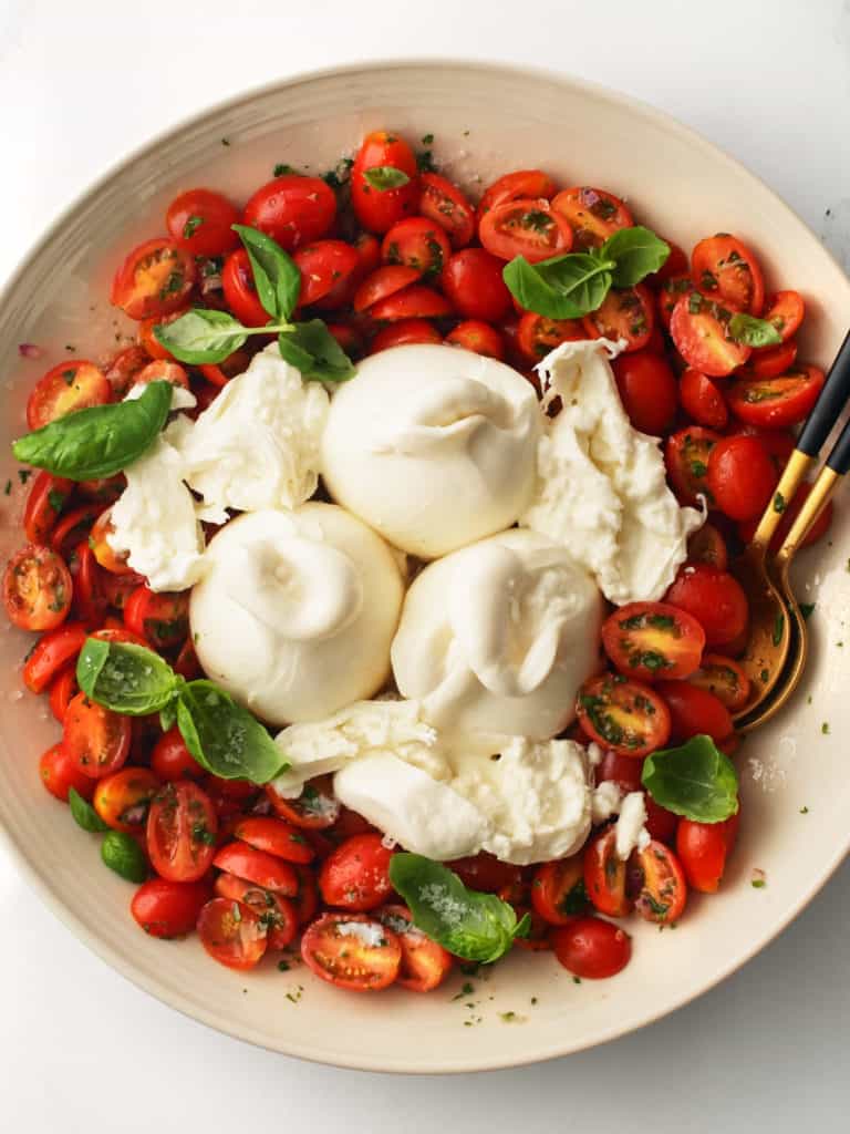 Fresh tomato, basil, burrata and herbs in a large serving bowl.