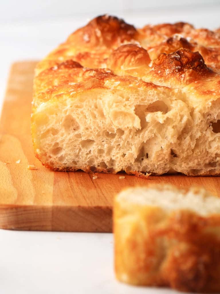 Focaccia slice exposed. sitting on a wooden cutting board.