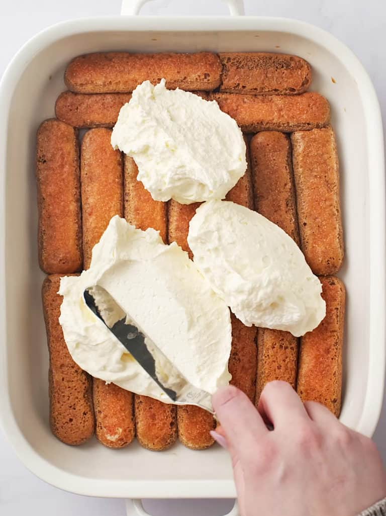 A baking trap full of coffee dipped lady fingers. Using a flat spatula to spread the cream filling.