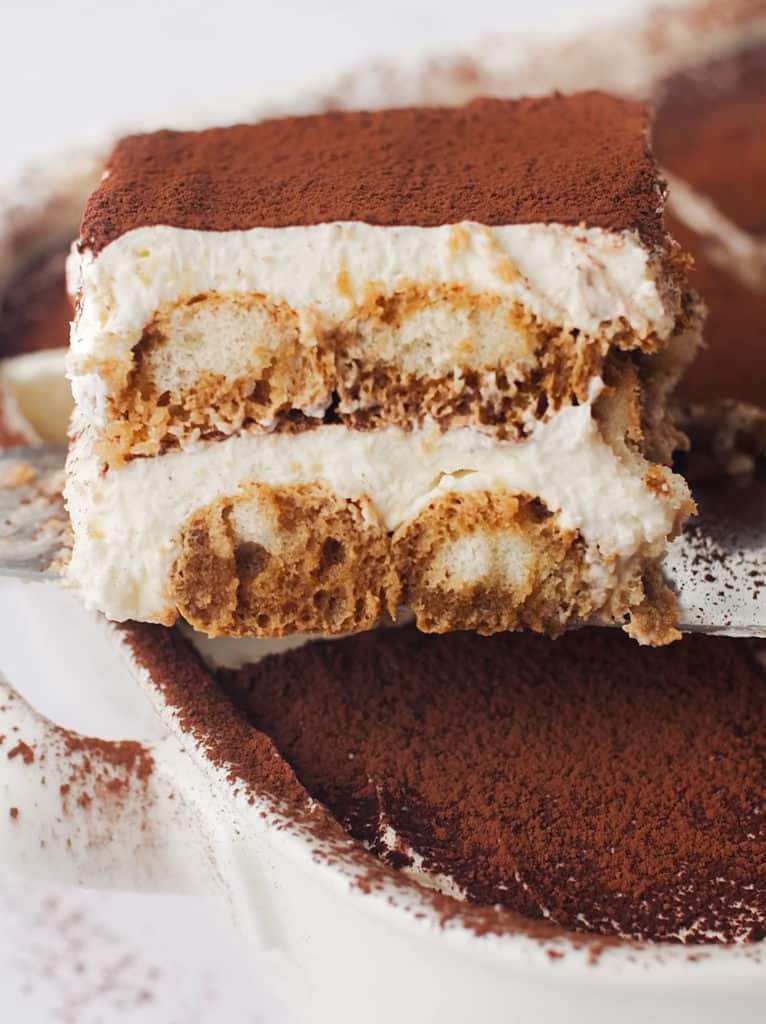 Tiramisu slice on a serving spatula with exposed layers of cream and lady fingers.