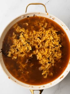 Dry pasta and beef broth cooking in large pan.