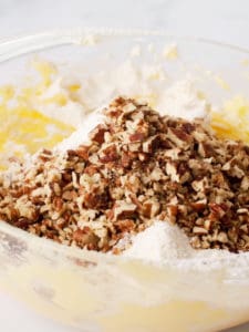 Large glass bowl with cookie dough, flour and chopped walnuts.