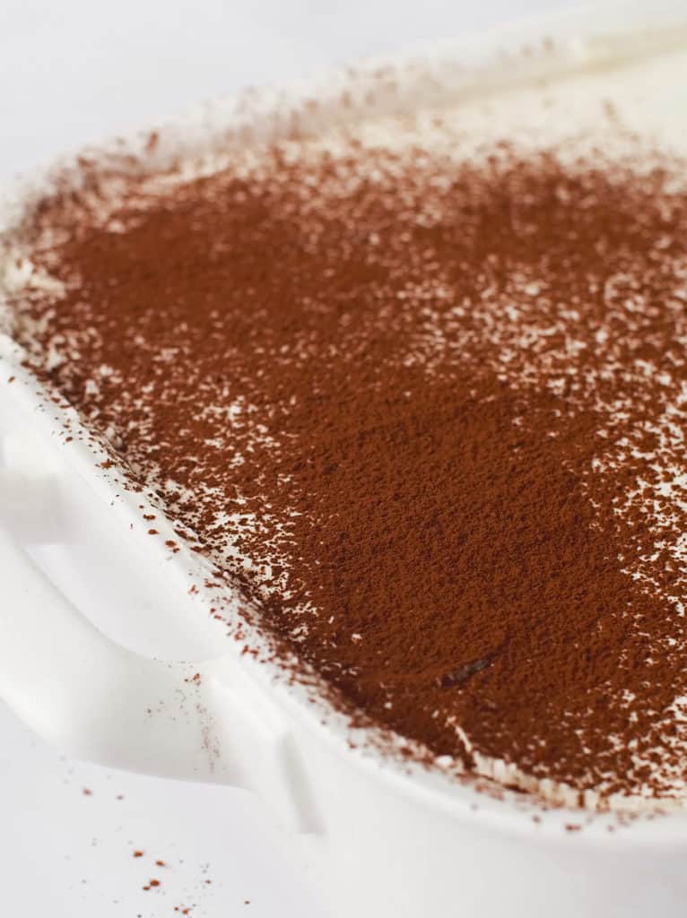 Layers of cream, lady fingers and cocoa powder in a large baking dish.