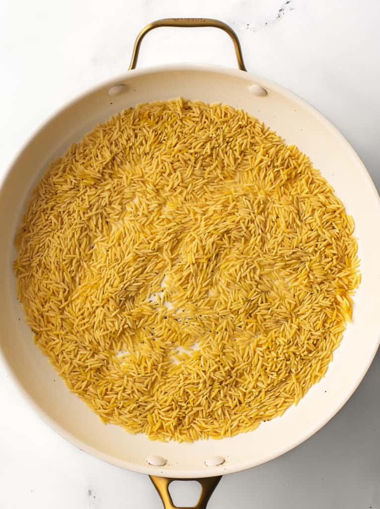 Orzo and cracked black pepper in cooking pan.