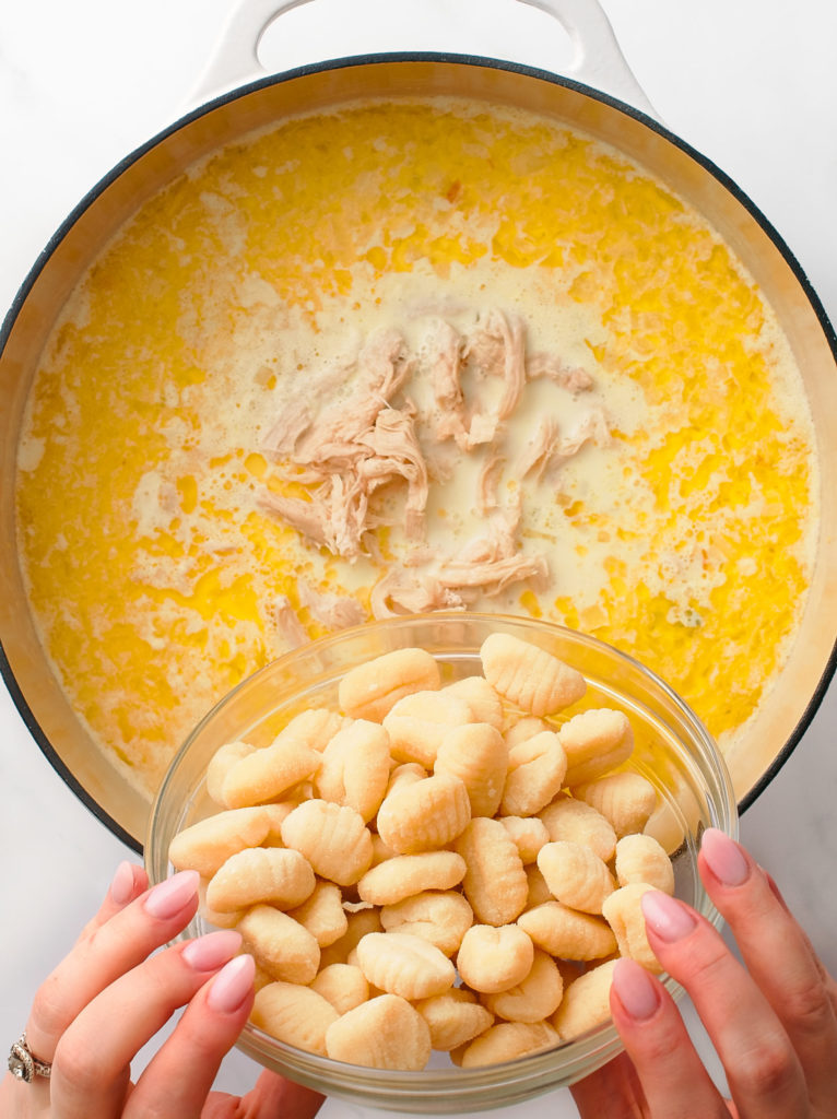 Pouring uncooked, dry gnocchi into large Dutch oven pot of soup.