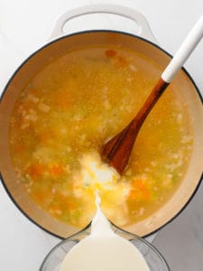 A large measuring cup adding half and half to a large Dutch oven pot of soup.