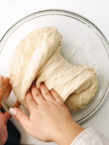 Using right hand to fold dough in a glass bowl.