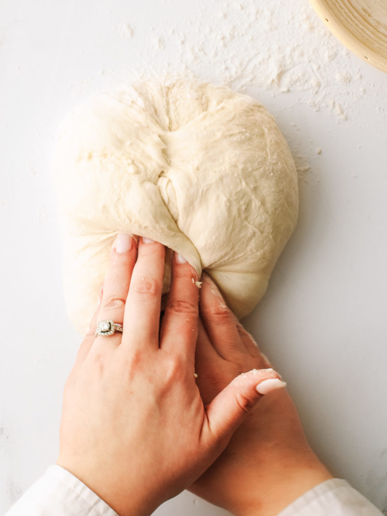 Using two hands to form the dough into a rough, round ball.