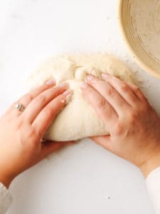 Using two hands to form the dough into a rough, round ball.