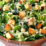 Caesar Salad arranged in wooden bowl with dressing and crispy croutons.