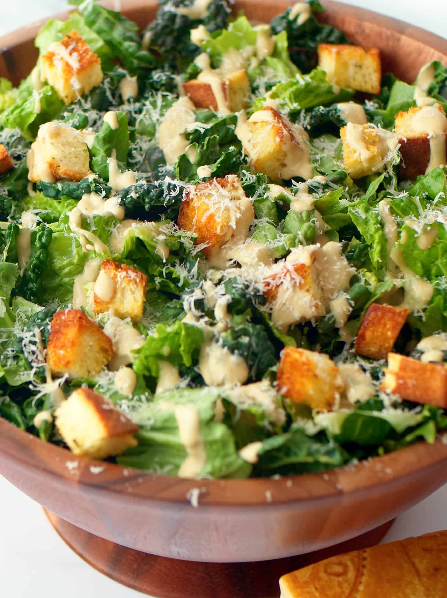 Caesar Salad arranged in wooden bowl with dressing and crispy croutons.