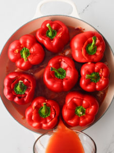 Traditional stuffed peppers arranged tightly inside a large skillet. Pouring tomato sauce over the peppers.