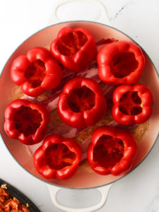 Hollow red bell peppers arranged tightly inside a large skillet.