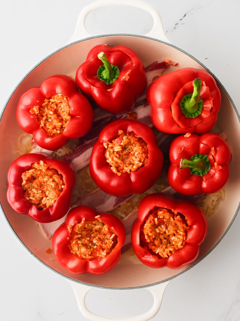 Red bell peppers with filling arranged tightly inside a large skillet.