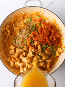 Chicken, noodles, peas, carrots, rice and chicken broth in a large pan.