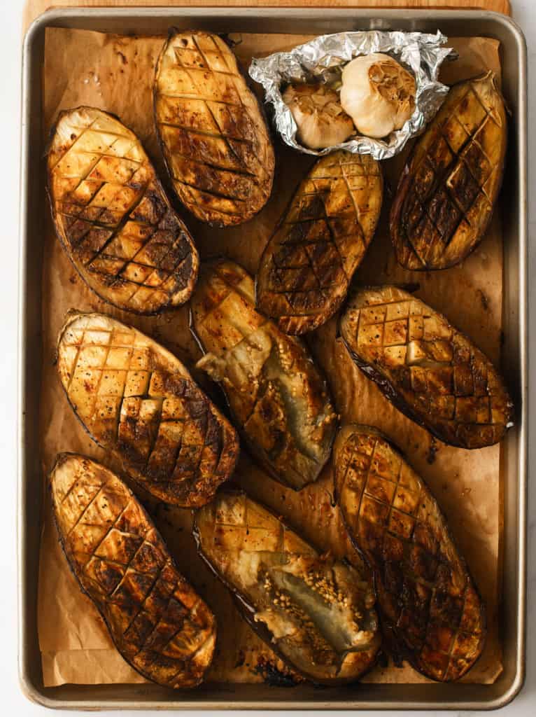 Roasted eggplants and garlic on baking tray.