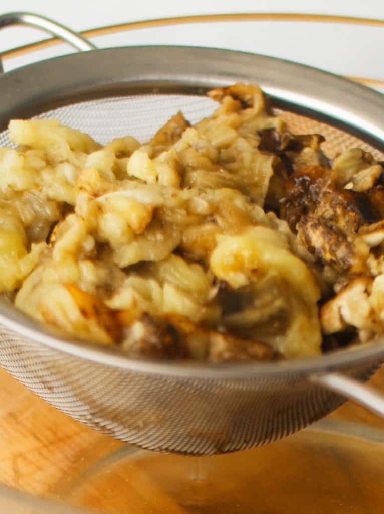 Roasted eggplant soft center draining in mesh strainer over a glass bowl.