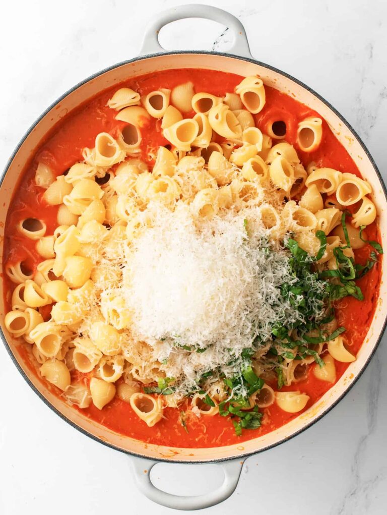 Pasta sauce in a large cooking pan with pasta, cheese and fresh basil leaves.