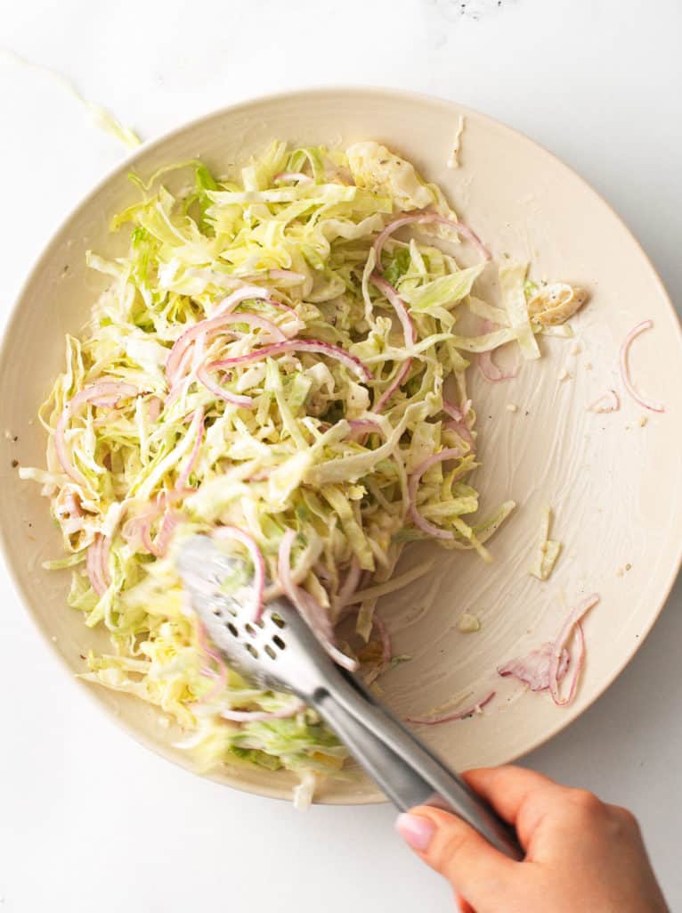 Combining creamy, salad dressing with lettuce and red onion.