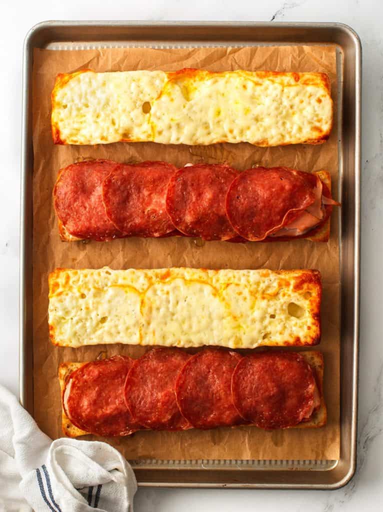Baguette loaves shown baked, with layer of cheese and crispy meat.