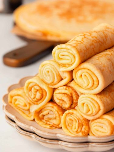 Crepes rolled into logs and stacked like a pyramid on a plate.