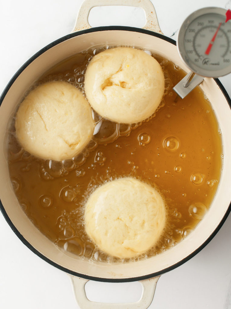 Brioche donuts frying in a large Dutch oven.