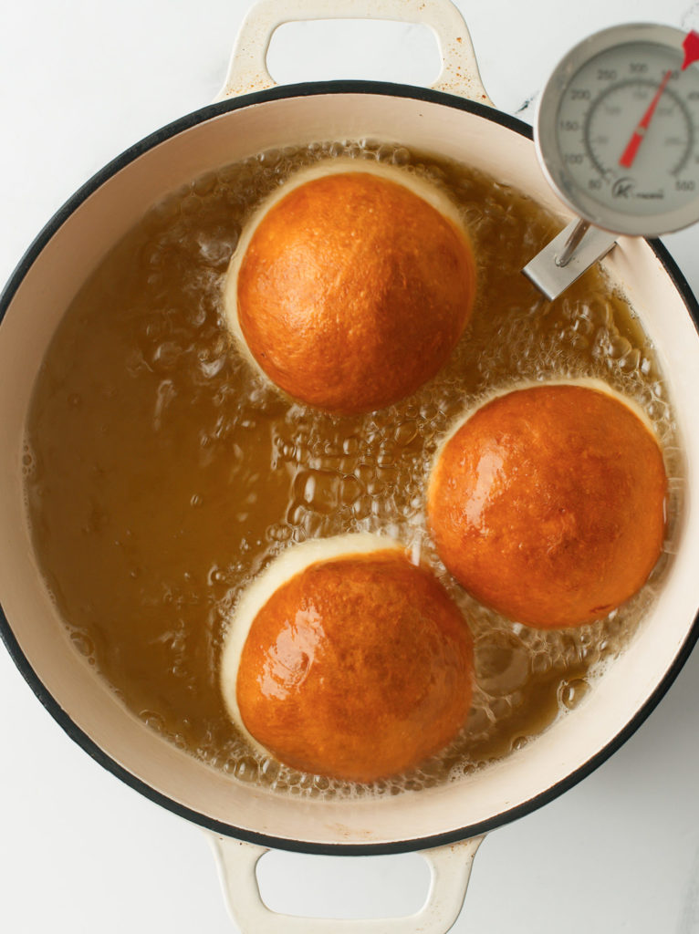 Brioche donuts frying in a large Dutch oven.