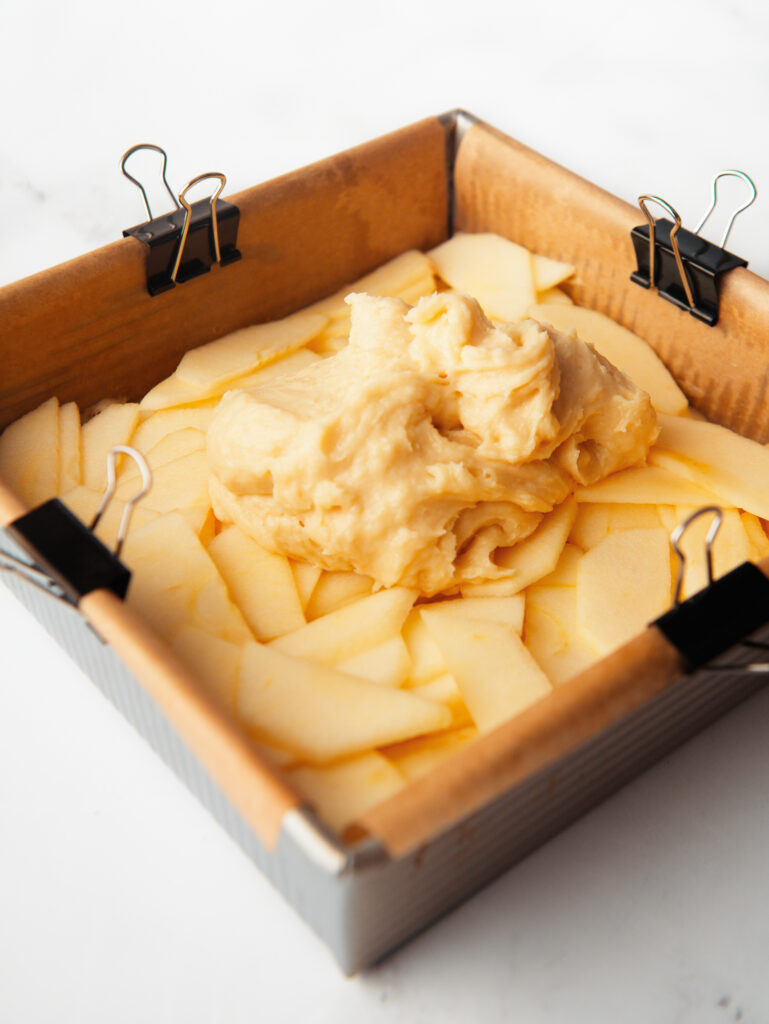 Layer of sliced apples and cake batter in square pan.