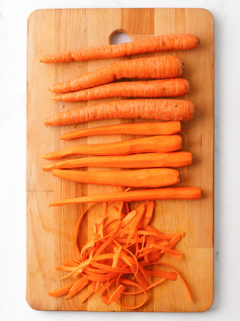 Peeled large carrots on a wooden board.