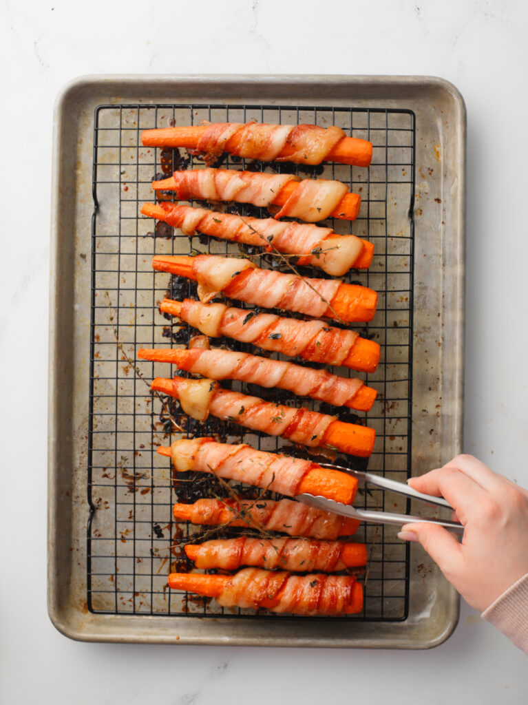 Flipping bacon wrapped carrots in baking tray.