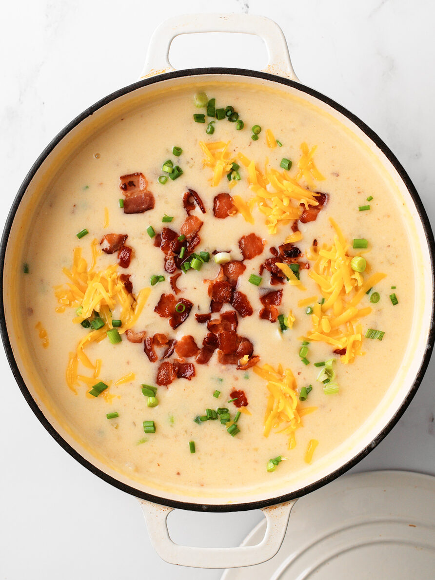 Finished soup in large Dutch oven pot with bacon, cheese and green onion toppings.