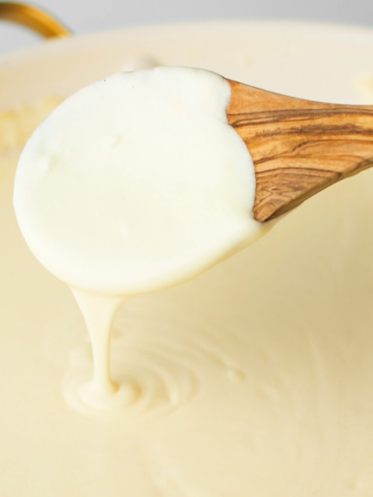 Wooden spoon stirring creamy alfredo sauce.