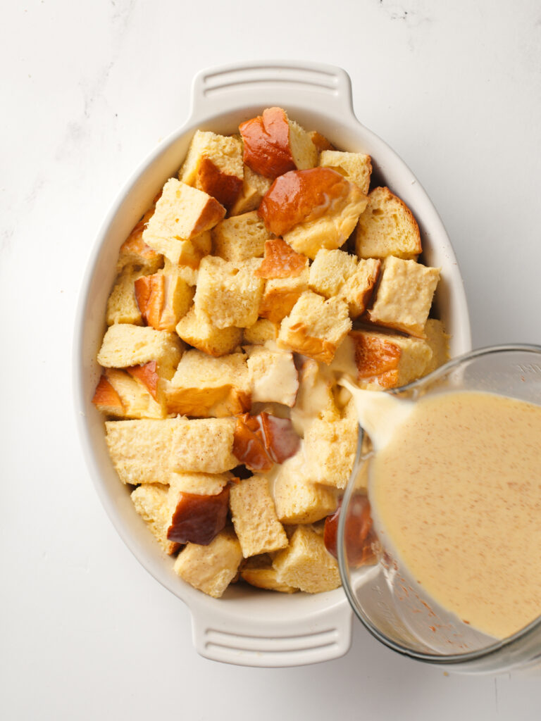 Pouring custard over brioche cubes in baking dish.