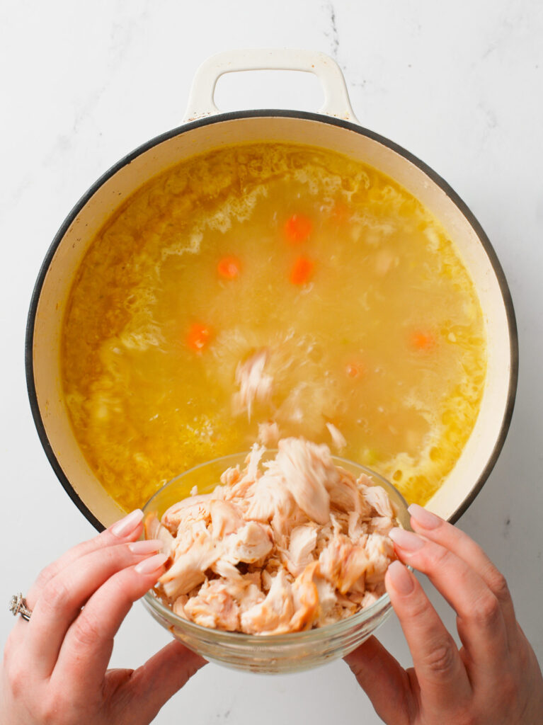 Pouring shredded chicken to soup pot.