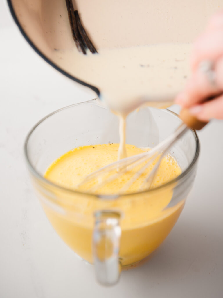 Whisking in warm milk to the egg mixture.