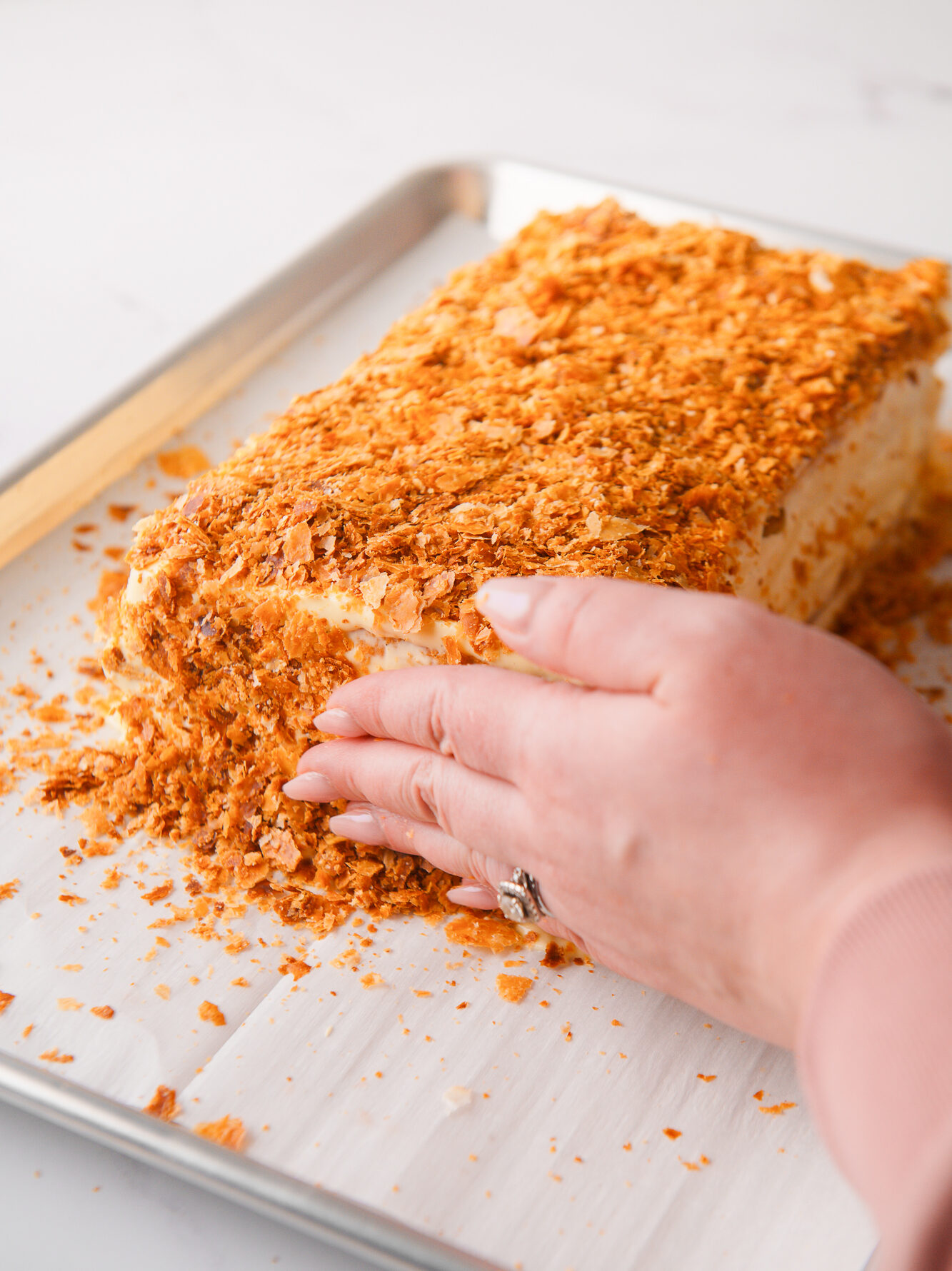 Pressing the sides of the cake with crushed puff pastry flakes.