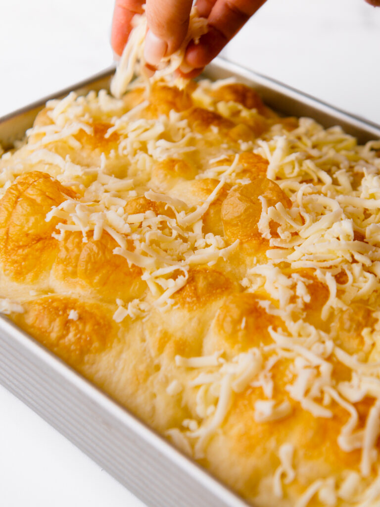 Sprinkling shredded cheese to the focaccia.