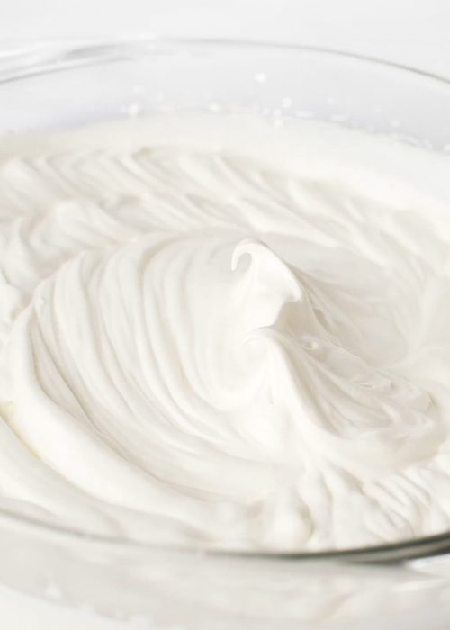 Whipped cream in a large, glass mixing bowl.