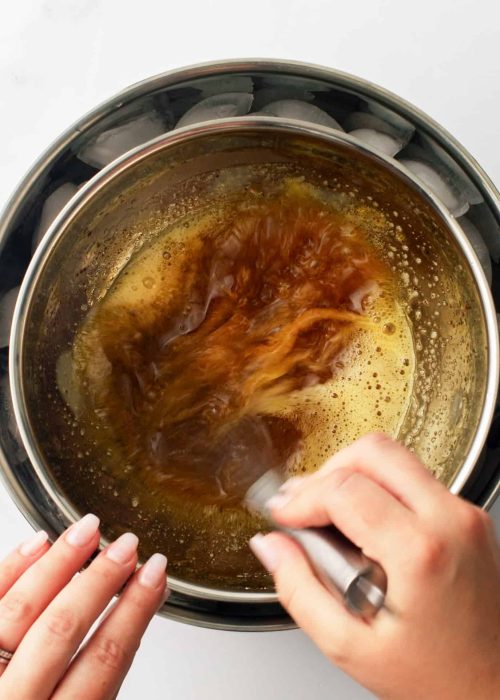 Using a whisk to whip melted brown butter in a smaller bowl over a larger bowl of ice.